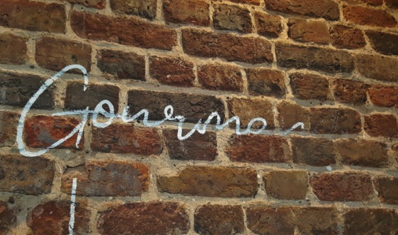 Brick wall signwriting in progress with script lettering and pounce pattern visible on exposed brickwork.