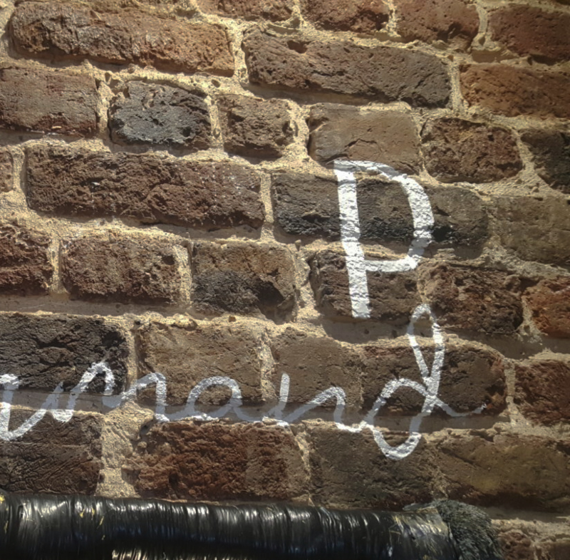 Business branding being painted onto exposed brickwork during a commercial interior fit-out in Soho.