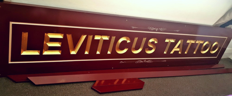 Carved wooden sign with completed 23ct gold leaf lettering, gilded border and hand-painted embellishments before frame assembly.