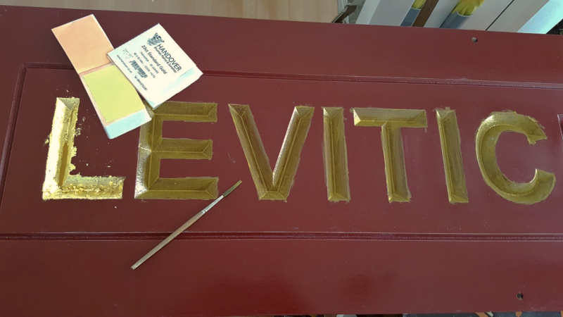 Genuine 23ct gold leaf being laid onto sized V-carved lettering on an Accoya wooden sign.