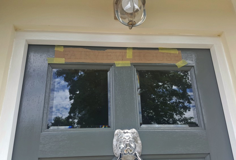 House name artwork being positioned on the entrance door before traditional hand painting in Enfield.