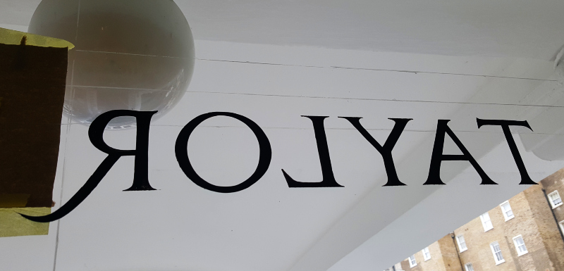 Traditional signwriter painting reverse glass lettering onto a transom window.