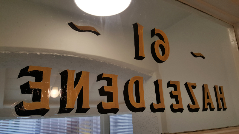 Applying protective varnish to reverse glass entrance lettering after completing the house name and property numbering.