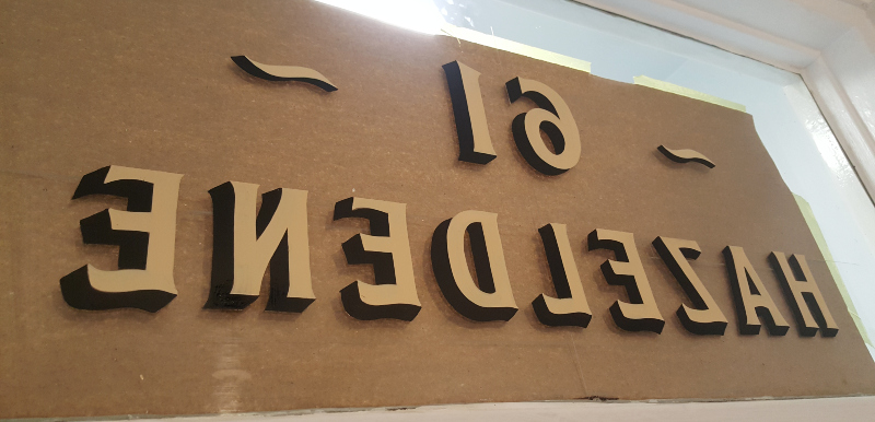 Hand painting the cast shadow onto reverse glass entrance lettering to provide subtle depth and definition.