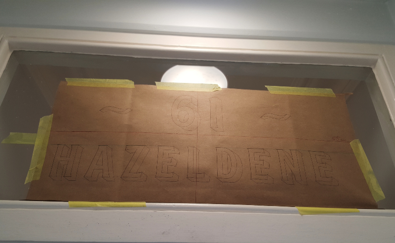 Full-size paper artwork positioned on the transom glass before transferring the entrance lettering.