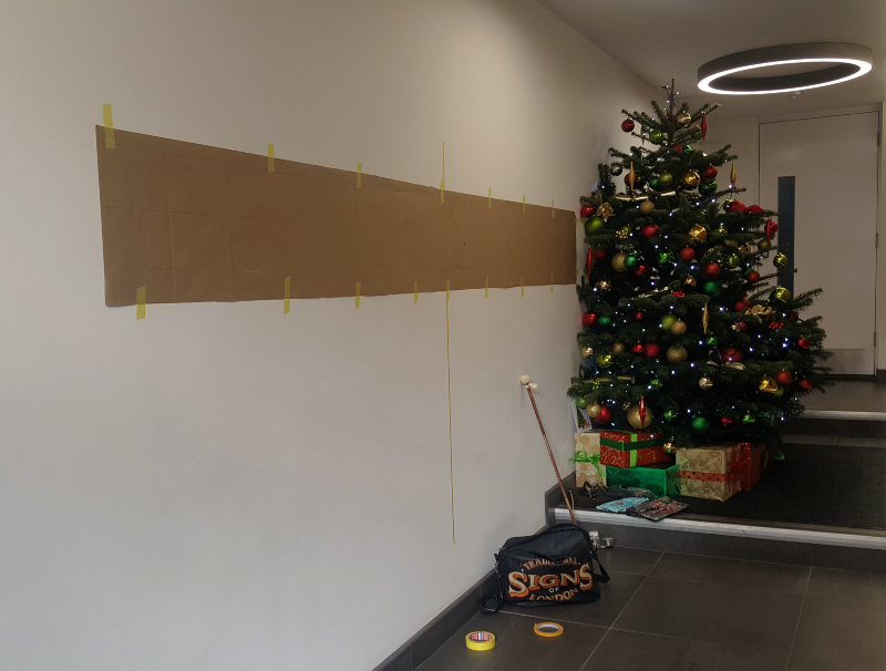 Measuring and positioning the full-size paper artwork before pouncing the address lettering onto the entrance wall.