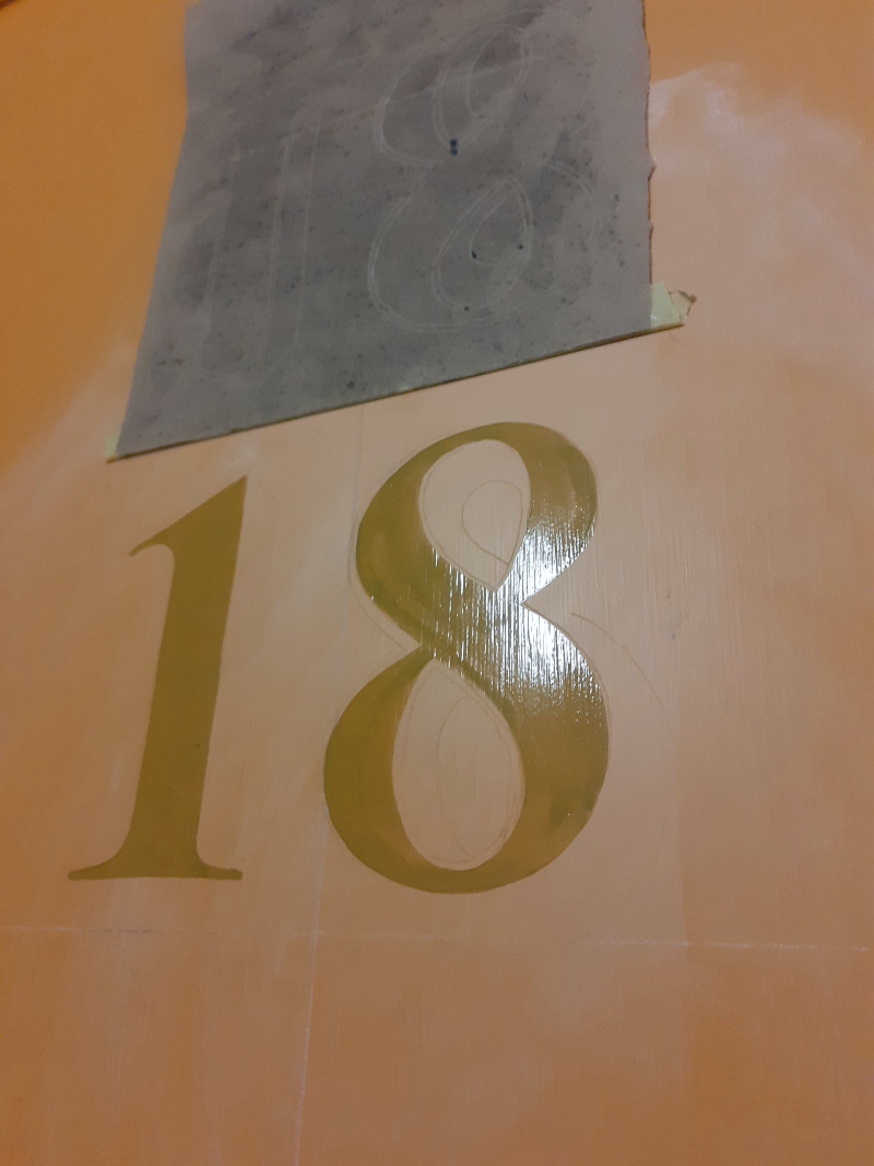 Applying traditional oil gilding size to apartment entrance numbering before laying genuine gold leaf.