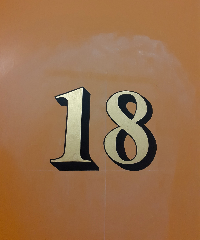 Hand painting the outline and cast shadow around genuine gold leaf apartment door numbering.