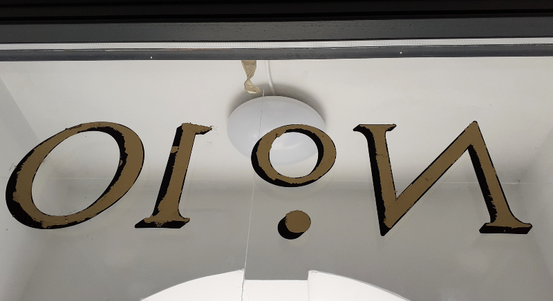 Laying genuine gold leaf onto reverse glass architectural property numbering using traditional gilding techniques.