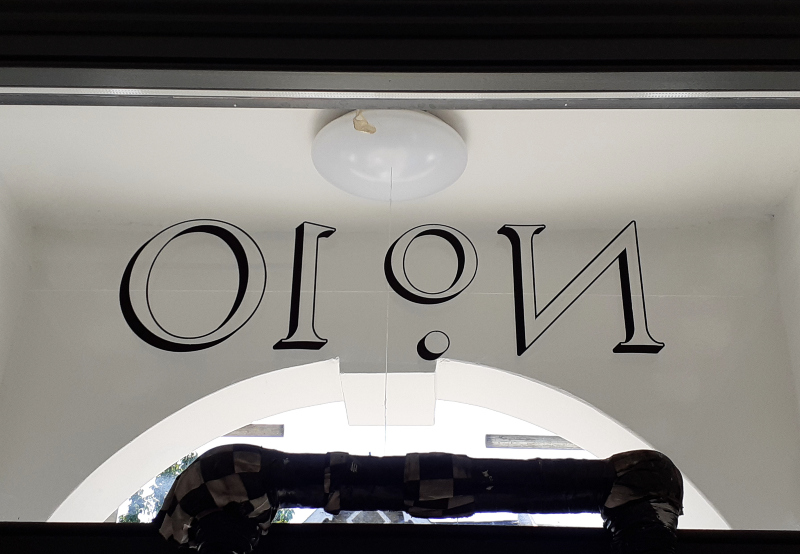 Painting the outline and cast shadow for genuine gold leaf property numbering on the glazed entrance of a period residence.