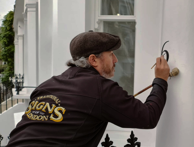Traditional signwriter hand painting bespoke house numbers for a distinguished residential property in London.